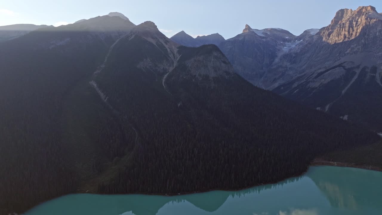 Ripresa cinematografica che rivela un bellissimo lago color smeraldo, circondato da alberi alti e montagne