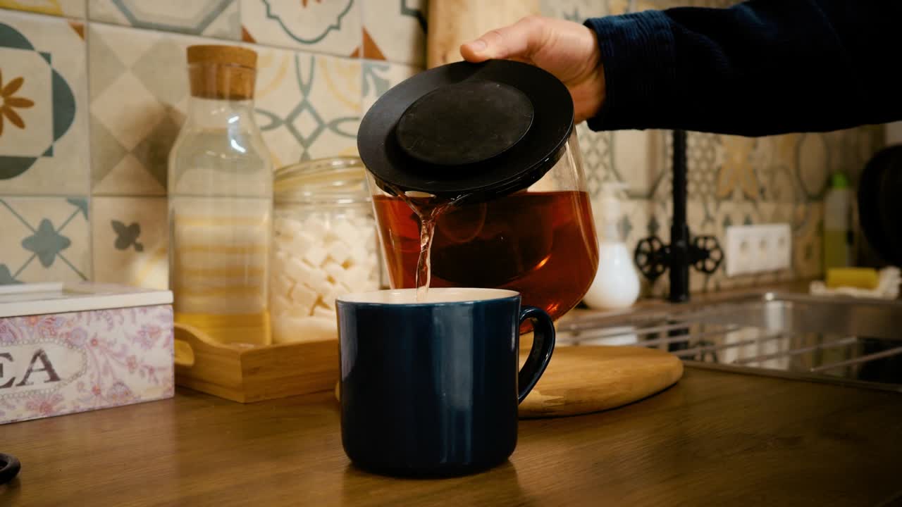 la mano de un hombre vierte té recién preparado en una taza. mañana soleada