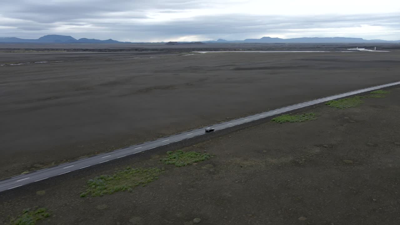 Driving a car through Iceland's vast plains with a 4K drone following a car amidst endless dirt and distant mountains