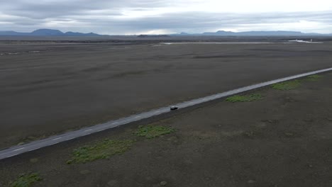conduciendo un coche a través de las vastas llanuras de islandia con un dron de 4k siguiendo un coche en medio de la suciedad sin fin y las montañas lejanas