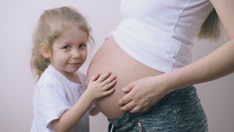 chica besa el estómago grande de la mamá embarazada escuchando al bebé