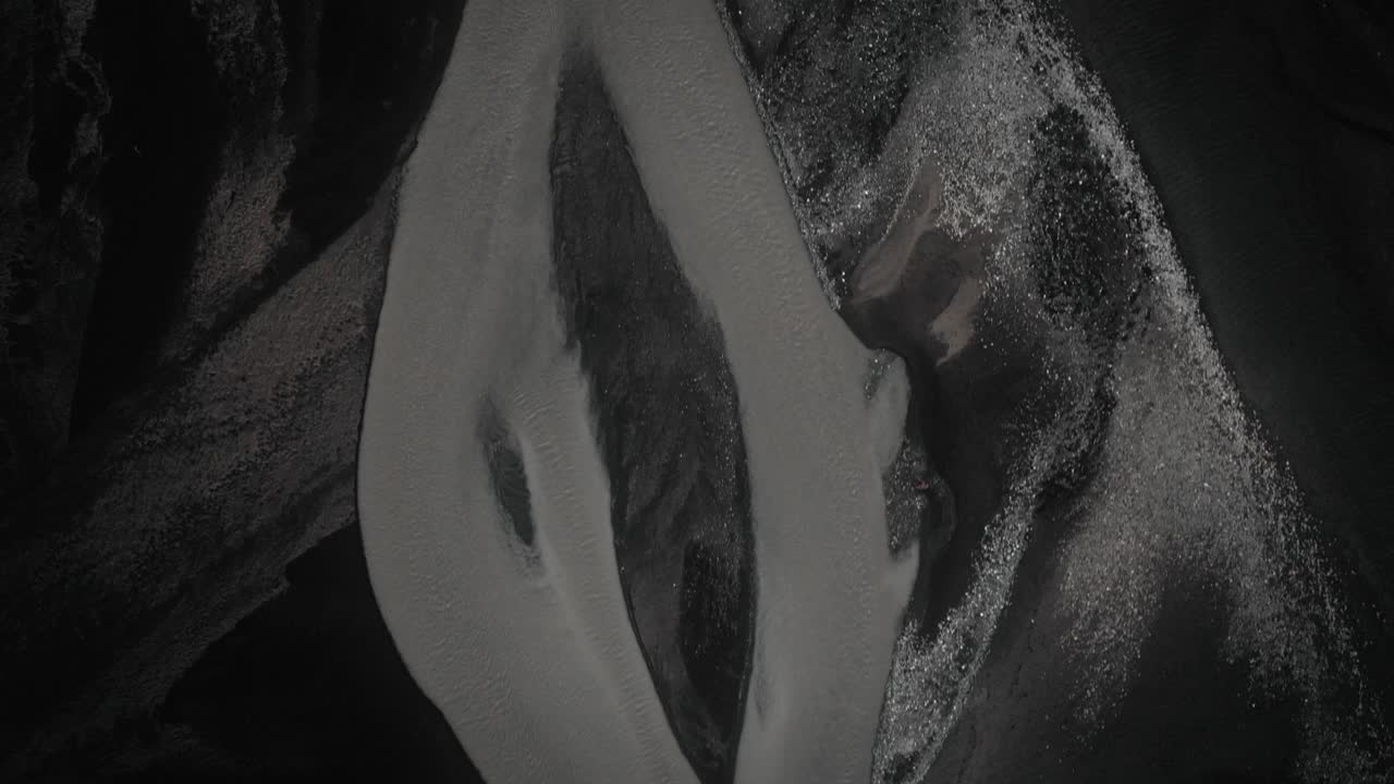 Aerial moody top down riverbed glacial river flowing through black natural volcanic landscape