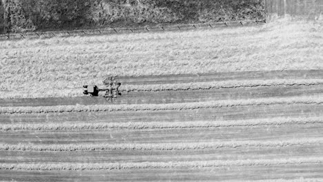 Tractor-Con-Su-Remolque-De-Rastrillo-De-Rotor-Doble-Trabajando-En-Una-Granja-Directamente-Desde-Arriba-En-Blanco-Y-Negro