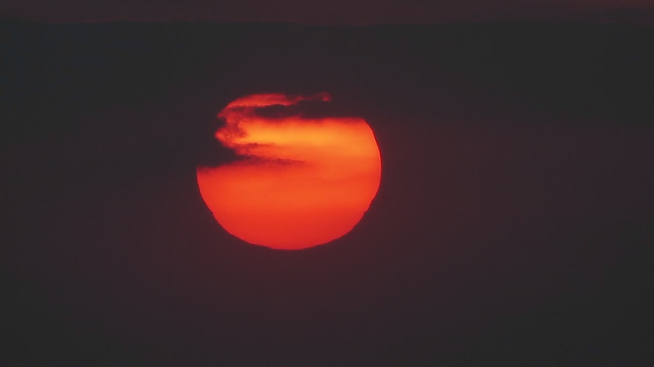 el sol se pone lentamente a través de las nubes en una enorme bola naranja