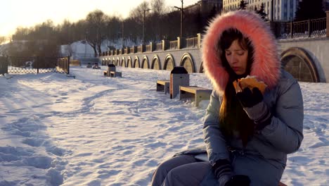 una mujer joven come una hamburguesa en la calle de invierno.