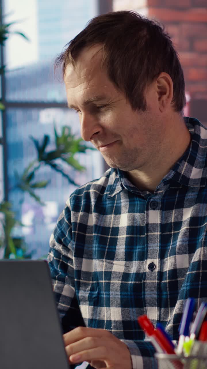 Vertical video Freelancer in home office at desk in front of laptop, answering phone call