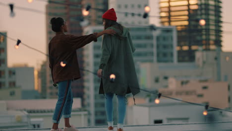 happy girl friends on rooftop with arms raised celebrating friendship enjoying hanging out together drinking alcohol embracing freedom looking at urban city skyline at sunset