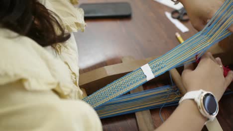 woman hand weaving patterns using blue and yellow