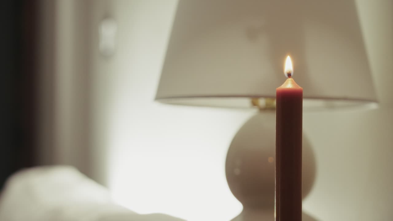 Una mano accende una candela in un ambiente interno, creando un’atmosfera calma e calda