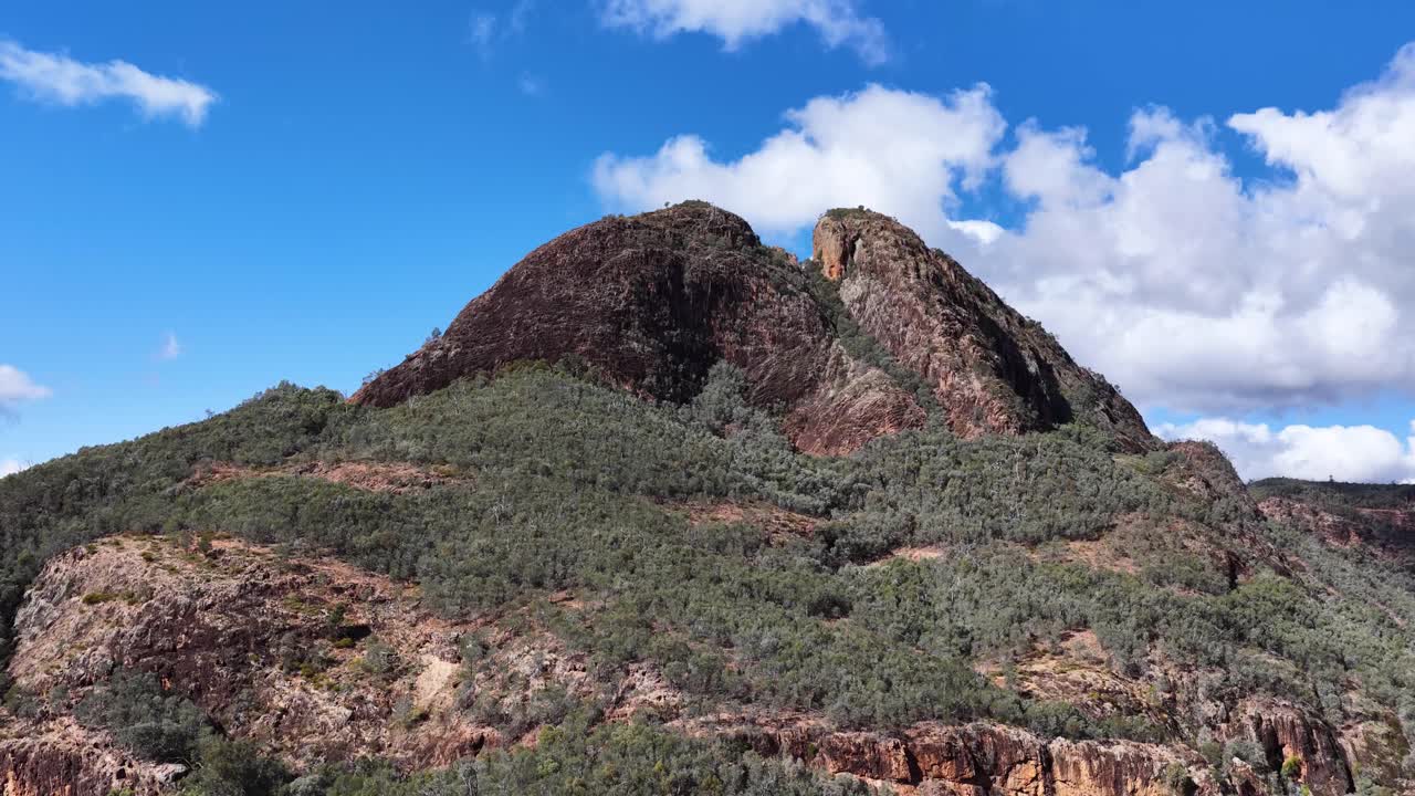 A daylight panning shot reveals Split Rock’s rugged peak, forested slopes, and dramatic sky in Warrumbungle National Park, Coonabarabran, Australia