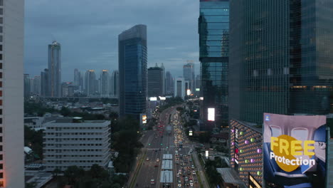 Aerial-dolly-shot-following-busy-car-traffic-in-downtown-city-center-surrounded-by-skyscrapers-of-Jakarta,-Indonesia