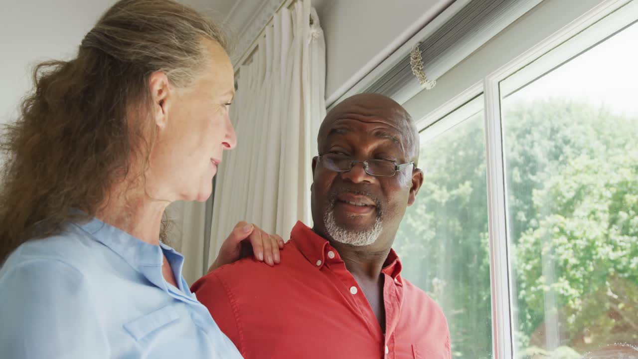 Happy senior diverse couple wearing shirts and embracing in living room
