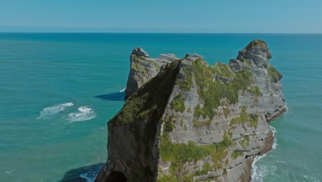 Vuelo-Aéreo-Sobre-Una-Formación-Rocosa-Salvaje-Y-Escarpada-Con-Un-Arco-En-El-Mar-De-Tasmania-En-El-Popular-Destino-Turístico-De-La-Playa-De-Wharariki-En-Cape-Farewell-En-Nelson,-Isla-Sur-De-Nueva-Zelanda-Aotearoa