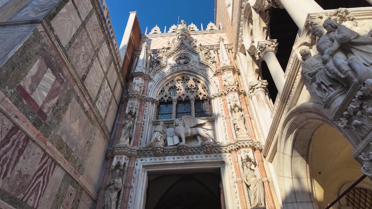 Vista in slow motion verso l'alto dell'ingresso riccamente decorato della Basilica di San Marco a Venezia, caratterizzato da intagli in marmo intricati, statue, colonne e dettagliati ornamenti architettonici.
