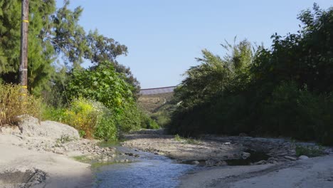 a tranquil stream meanders through lush greenery, approaching a distant border fence—a serene juxtaposition of nature and human-imposed boundaries