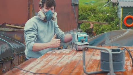 young man thumbs up satisfied with sanding job boat roof