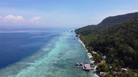drone aéreo que se eleva sobre el alojamiento de la cabaña de playa con vistas al arrecife de coral en el exótico destino de buceo de raja ampat en papúa occidental, indonesia