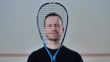 man lifts squash racket in front of face, smiling in creative sports portrait