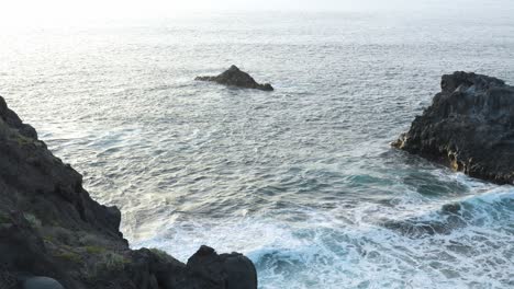 Slow-motion-shot-of-waves-splashing-against-rocky-coast-in-Los-Gigantes,-sunset