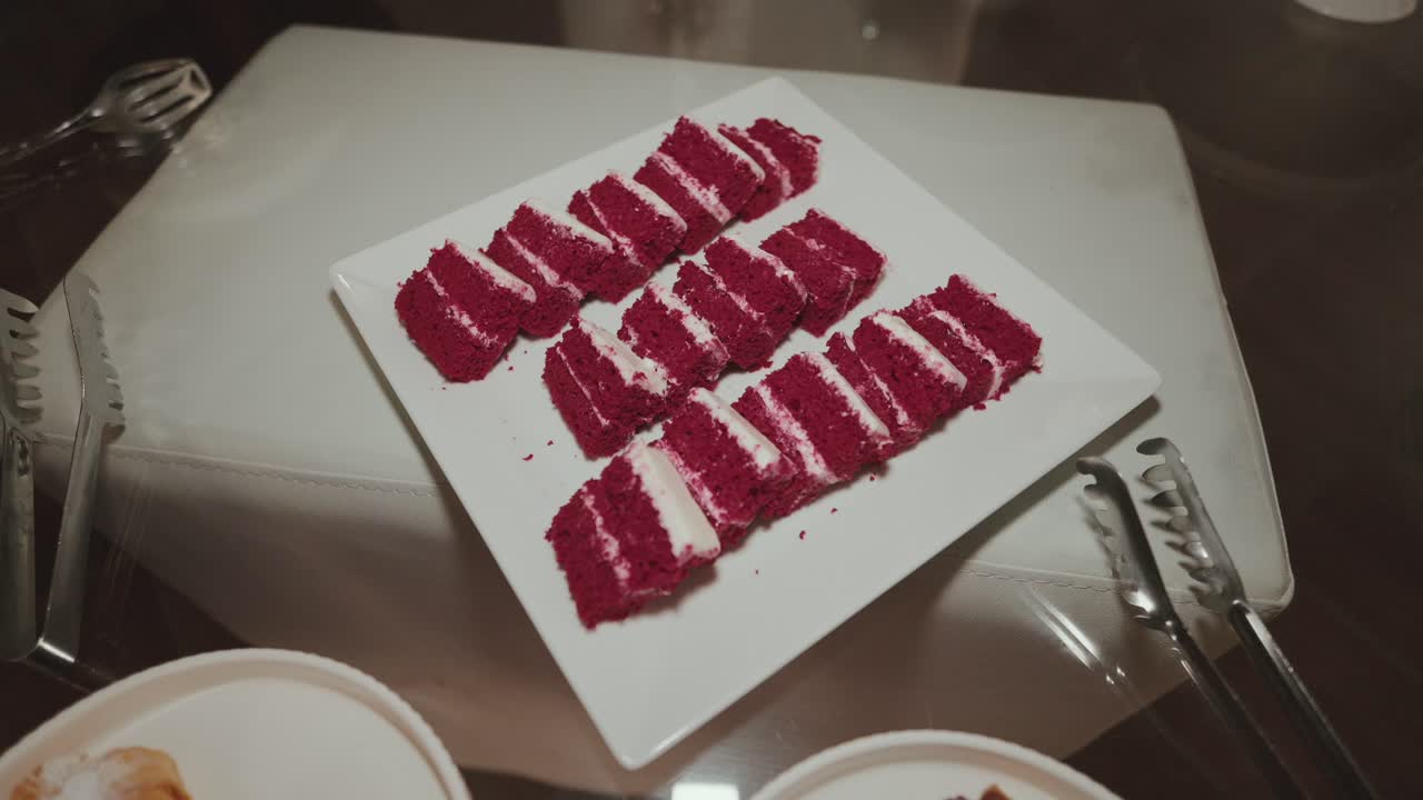 Close up of neatly sliced red velvet cake with cream filling arranged on white square platter