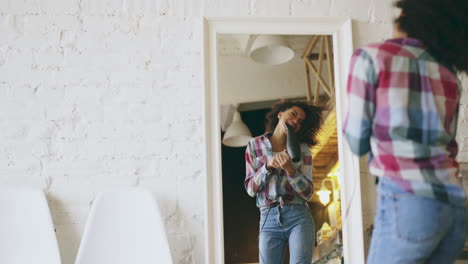 young woman drying her hair and having fun in front of a mirror