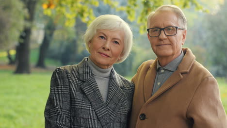 senior man and woman looking at each other with love, then they look at camera and smile at sunset in the park in autumn