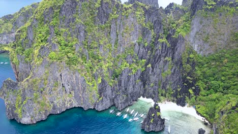 Aerial-overview-of-bangka-boats-anchored-at-mouth-of-deep-blue-bay,-el-nido