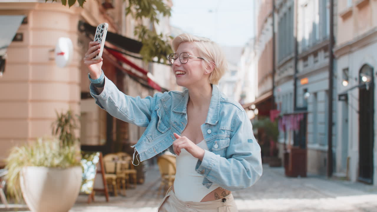 Cheerful young woman smiling friendly at camera waving hands gesturing while standing on city street