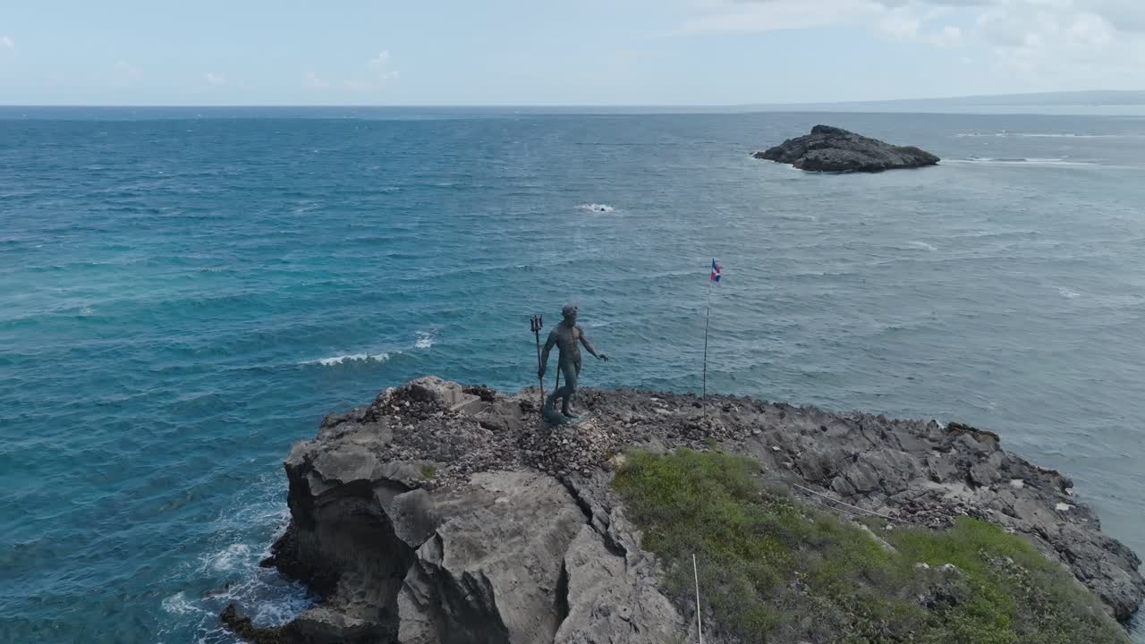 Neptune statue on rocky outcrop in ocean, Dominican flag, Puerto Plata in Dominican Republic. Aerial drone orbiting