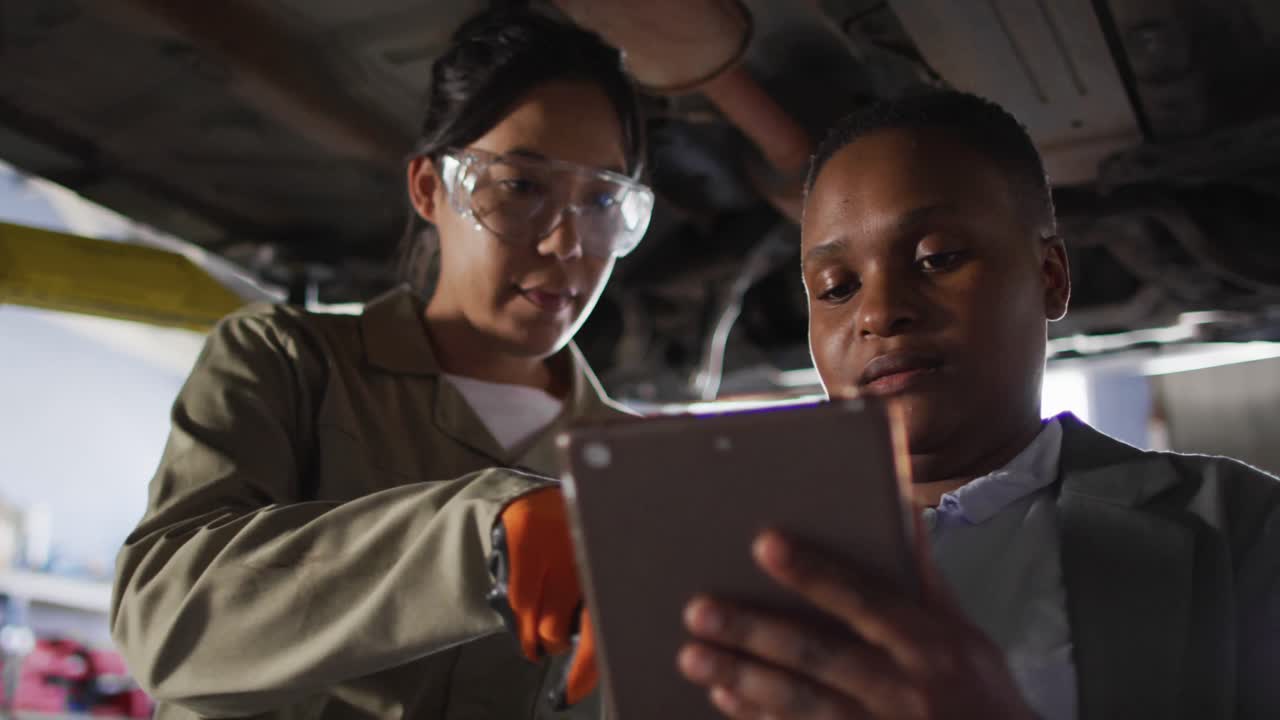 Video of two diverse female car mechanic and business owner with tablet checking car