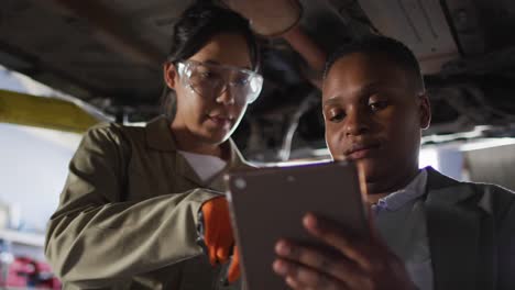 video of two diverse female car mechanic and business owner with tablet checking car