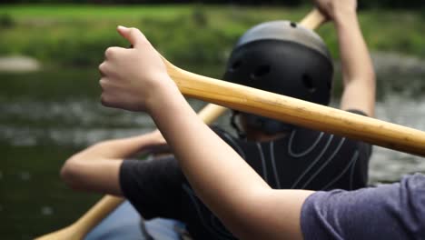 slowmo - two white kids paddle canoe with helmets and pfd on pelorus river, new zealand with beautiful nature in background - behind shot