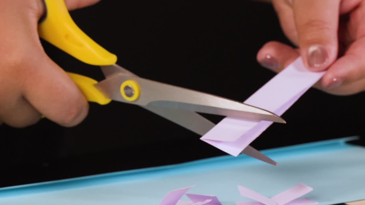 Primo piano di mani che usano forbici gialle per tagliare piccole strisce di carta viola