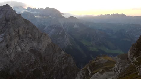 Vista-Aérea-De-Los-Acantilados-Y-Montañas-De-Linthal-En-Glarus,-Suiza-Durante-La-Puesta-De-Sol-Con-Pan-Desde-El-Valle-Hasta-Los-Picos-De-Las-Montañas-Con-Glaciares