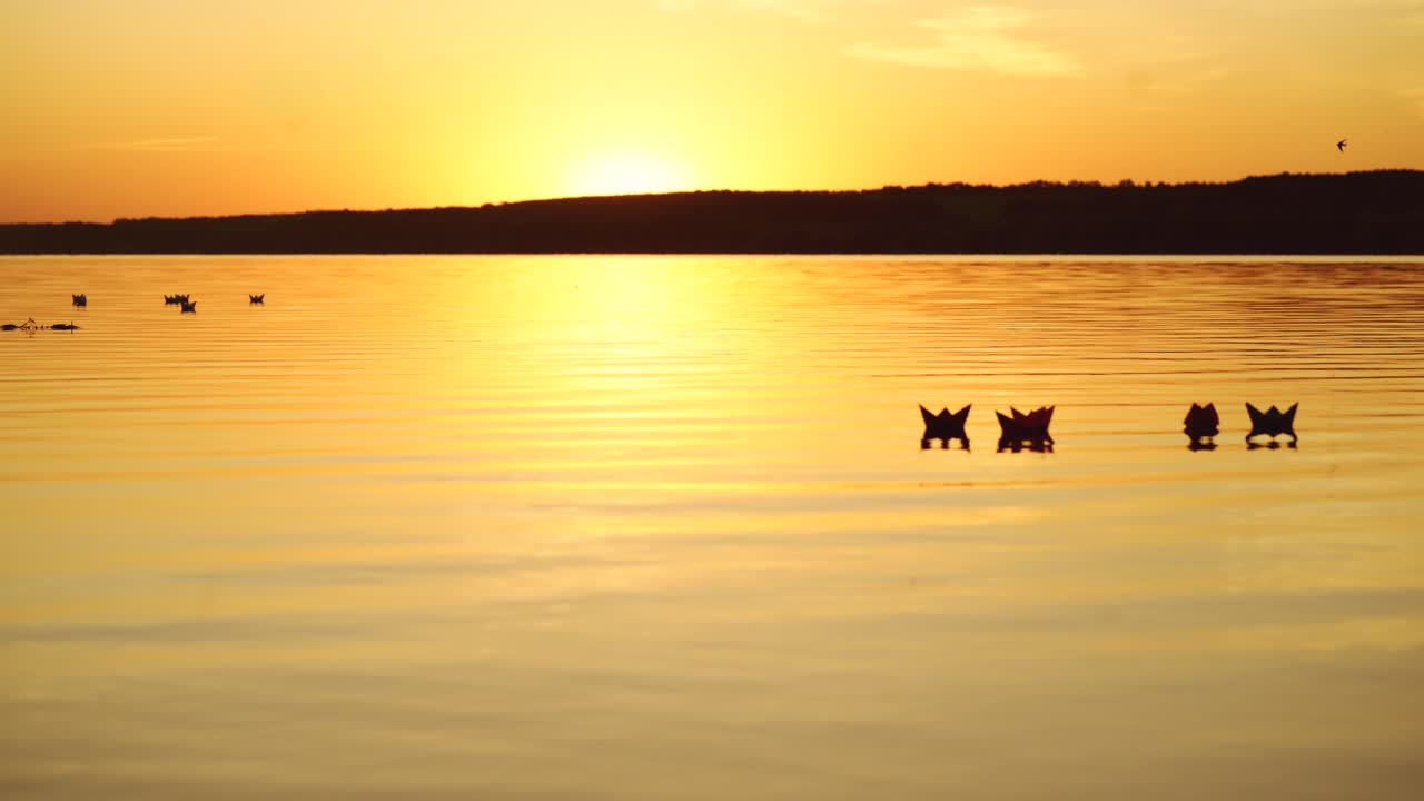 Good sunset with the reflection in the water and many paper boats floating in the river. Origami ships on water in the evening