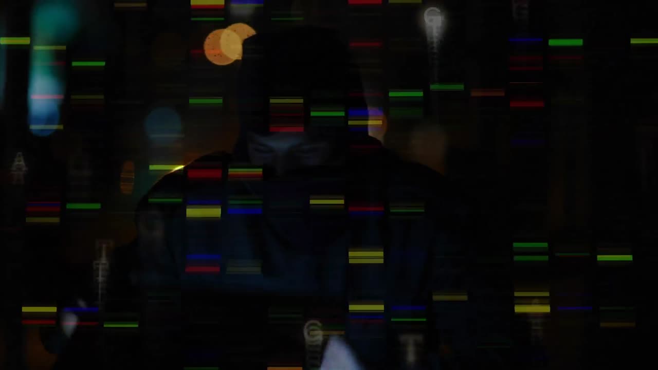 Hacker wearing balaclava using computer in a dark room with colourful digital lights on the foregrou