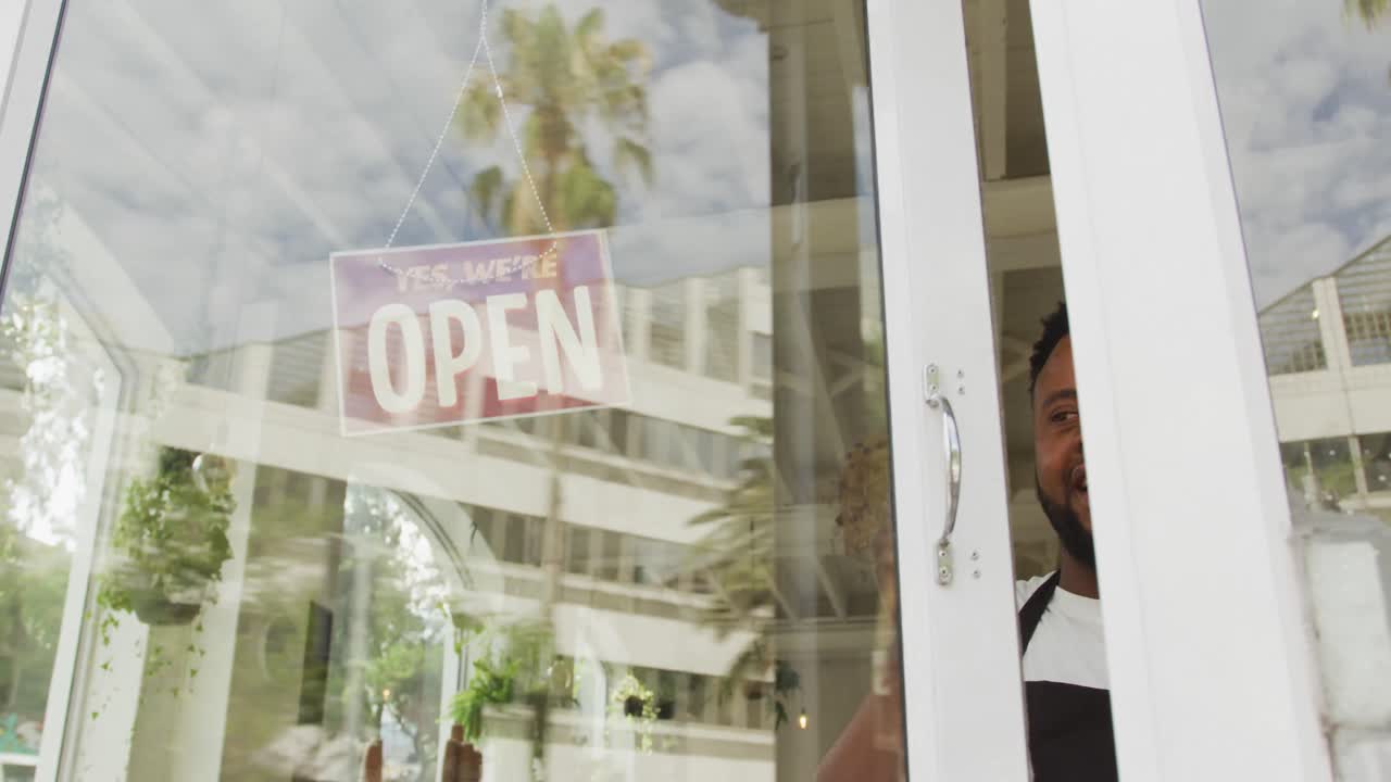 barista afroamericano feliz con un delantal negro abriendo un café y sonriendo