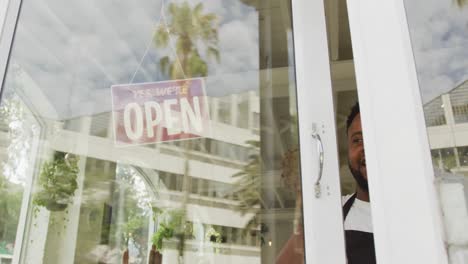 happy african american male barista wearing black apron opening cafe and smiling