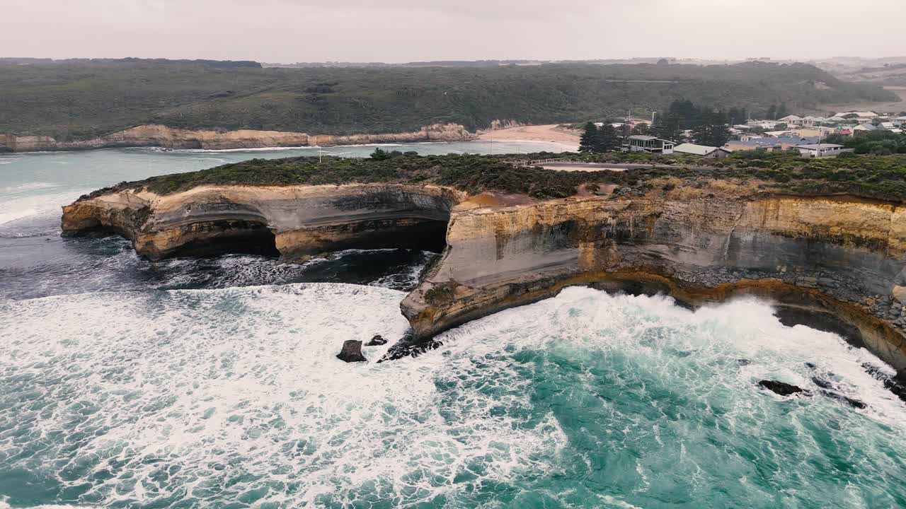 Drone footage captures dramatic cliffs and turbulent seas at Port Campbell, Australia. Overcast skies enhance the rugged, natural beauty