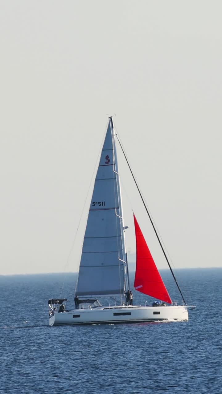 Una barca a vela con una vela rossa vivace scivola su un oceano blu calmo sotto un cielo sereno.