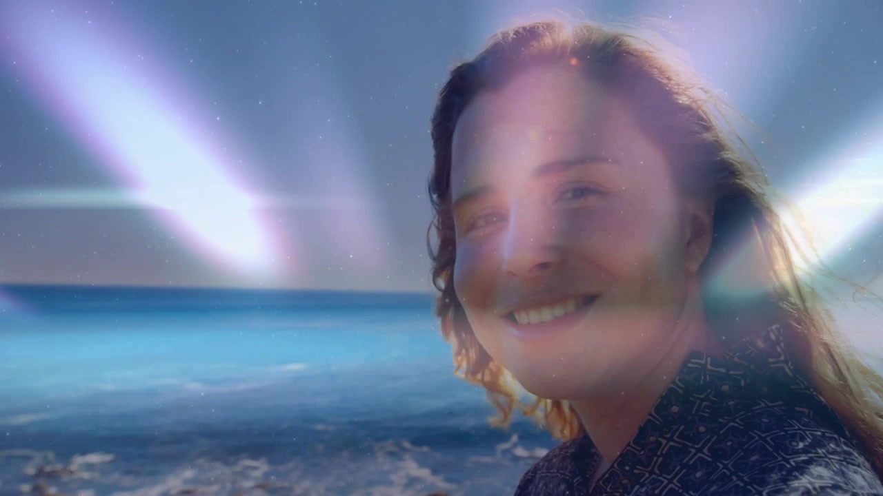 Donna che sorride sulla costa, con raggi di luce che attraversano l'orizzonte e le illuminano il viso, causando un'inclinazione della testa, per marketing.
