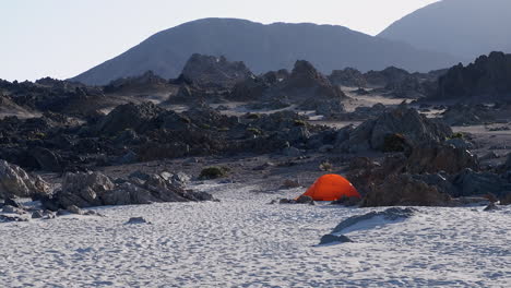 una tienda de color naranja sola en una escarpada playa de arena rocosa en la remota costa de chile