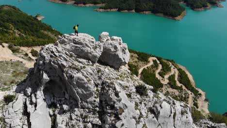 aerial-view-of-independent-adventurer-traveler-standing-on-top-of-a-rock-cliff-with-stunning-view-over-Bovilla-Reservoir