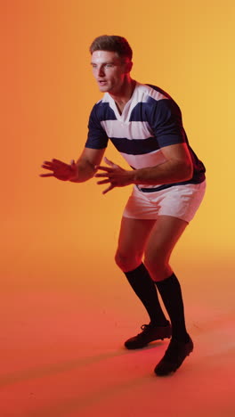 video vertical de un jugador de rugby caucásico atrapando una pelota de rugby sobre la iluminación rosa