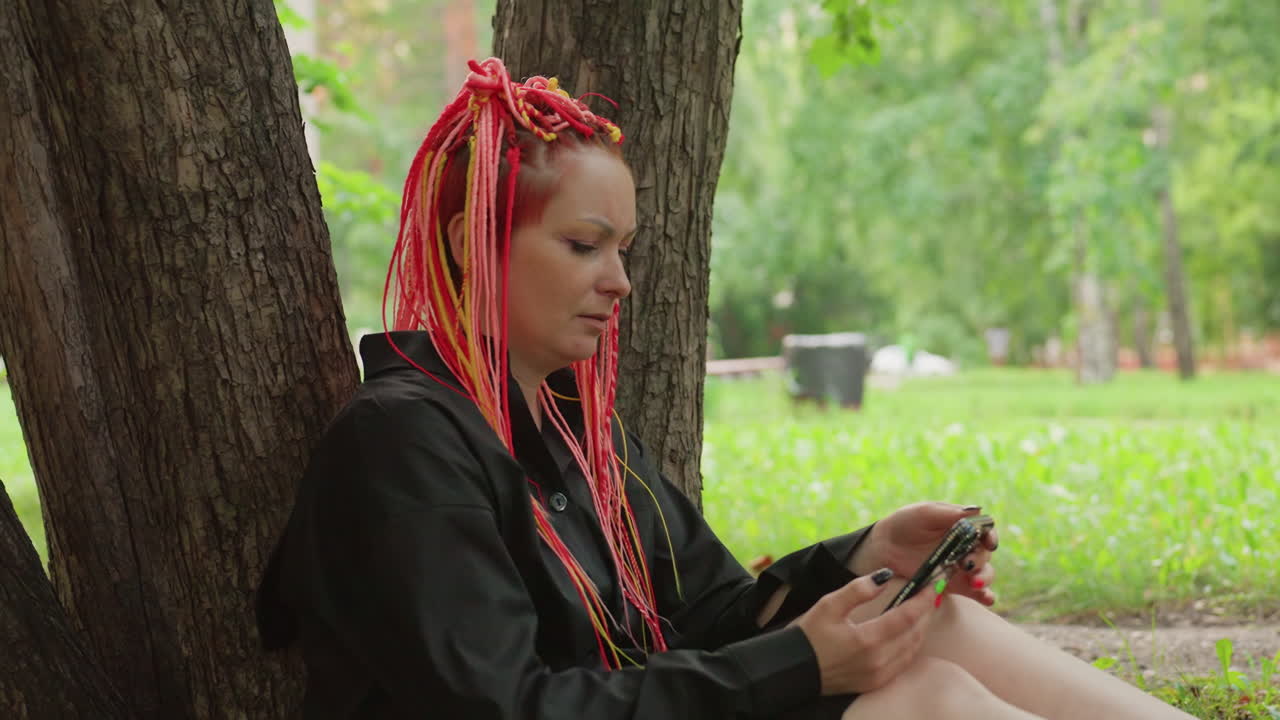 Человек спокойно изучает сообщения на природе; человек задумчиво просматривает сообщения в природном парке; европеец увлеченно читает сообщения в спокойной обстановке на открытом воздухе.