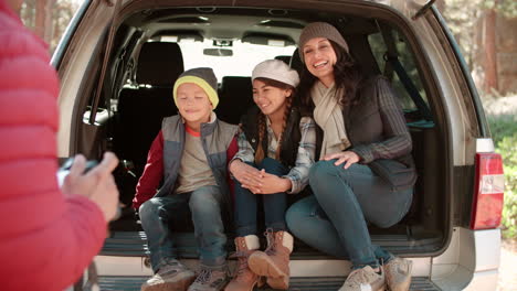 family looking at photos on a camera in the open back of car