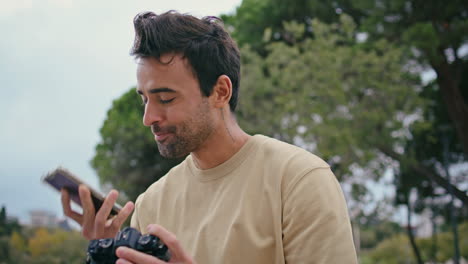 fotógrafo alegre hablando teléfono móvil en el parque de cerca. hombre mirando foto