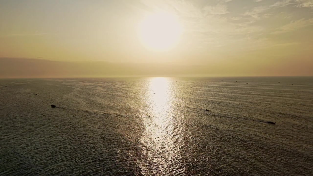 Aerial drone shot of the sunrise over the Bay of Bengal as golden sunlight reflects across the calm sea with fishing boats near Chennai in Tamil Nadu, India
