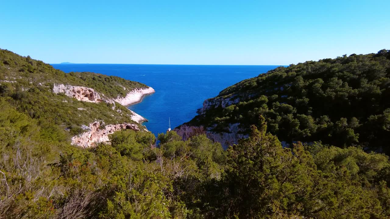 Splendida ripresa panoramica di un turista che cammina su un'isola tropicale con il mare che scorre tra le cime e una vegetazione lussureggiante su entrambi i lati. Spiaggia di Stiniva, isola di Vis, Croazia. Viaggio durante la pandemia di Covid.