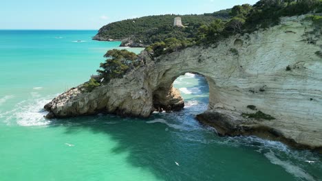 stunning 4k drone footage of a natural sea arch, limestone cliffs, and turquoise waters along the gargano coast in puglia, italy